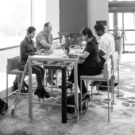 black and white image of people working on laptops at a counter height table on stools at the annual BRAIN meeting